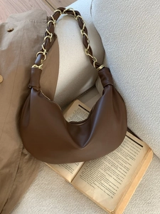 Sac hobo marron foncé minimaliste avec chaîne dorée posé sur un canapé beige doux