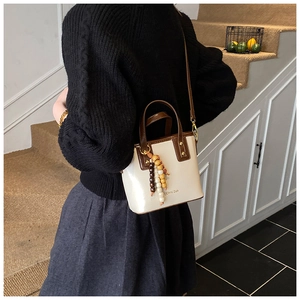 Mannequin portant un sac seau crème avec garniture en cuir marron et pendentif perles