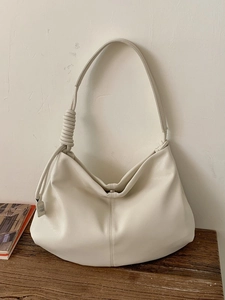 Minimalist beige soft leather tote bag with knotted strap on dark wooden surface