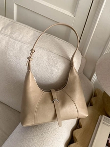 Borsa hobo minimalista beige in pelle con fibbia in metallo su un divano color crema