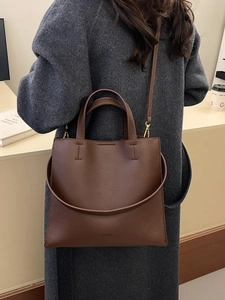 Brown lychee leather tote bag with gold hardware shown on a model in a minimal urban setting