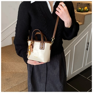 Détail d'un sac seau crème avec poignée marron, logo doré et perles en bois décoratives
