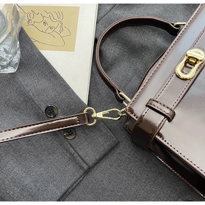 Dettaglio dei ganci dorati e del manico in pelle marrone lucida di una borsa a tracolla