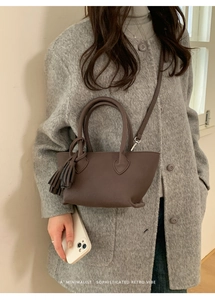 Deep brown pebble leather crossbody bag with tassel detail styled on a wool coat