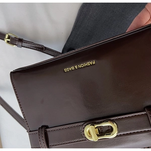 Dettaglio borsa a tracolla in pelle marrone con chiusura girevole dorata e logo stampato