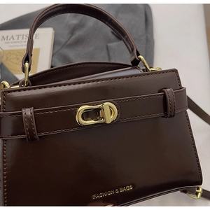 Dettaglio borsa in pelle marrone scuro con chiusura a scatto dorata e logo minimalista