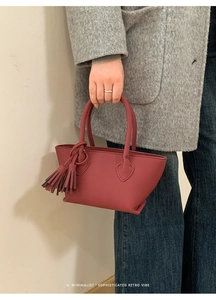 Chic burgundy leather handbag with fringe detail shown against a wool coat background