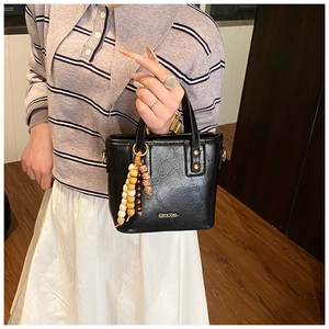 Détail du sac seau en cuir noir avec lettrage doré et breloque en perles colorées