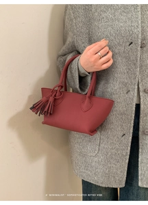 Detail of dark red leather bucket bag with long tassels and elegant handheld design