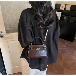 Modella che indossa una borsa a tracolla in pelle marrone scuro con fibbia dorata e scritte