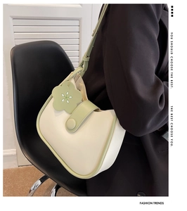Fashionable cream and green contrast shoulder bag with flower charm shown on a model