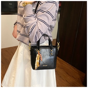 Détail du sac seau noir en cuir PU avec charm en perles de bois et accessoires dorés