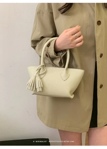 Close-up of a minimalist cream-colored leather mini tote bag with tassel detail held by model