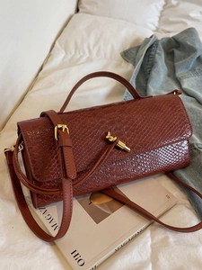 Sac bandoulière marron foncé effet crocodile avec fermoir doré sur draps blancs
