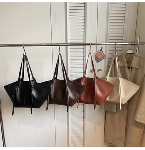 Four vintage tote bags in black, brown, tan, and cream hanging on a metal rack