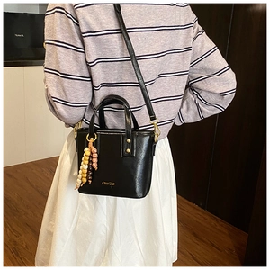 Détail d'un sac seau en cuir noir avec breloque en perles de bois et logo doré