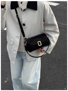 Detail of a black suede crossbody bag with a vintage gold rectangular clasp and strap