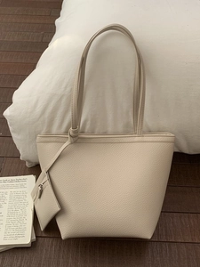 Minimalist cream leather tote bag with long straps and matching pouch on wood floor
