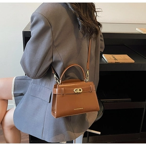 Dettaglio borsa a tracolla in pelle marrone con chiusura a scatto dorata e scritte moda