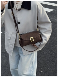 Detailed view of a dark brown square crossbody bag with gold buckle on a model