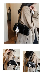 Detail of black faux leather shoulder bag featuring a floral charm and metal buckle