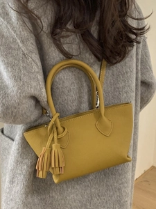 Mustard yellow minimalist top handle bag shown as a crossbody on a model with long coat