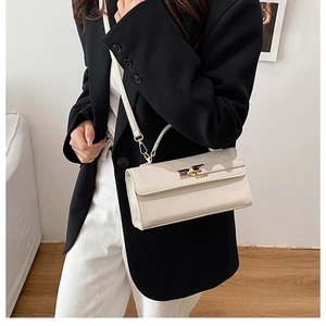 Close-up of cream rectangular handbag with gold metal twist lock and crossbody strap
