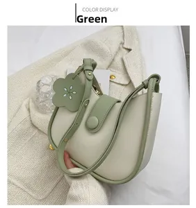 Detail view of half-moon bag in cream leather with green piping and floral charm