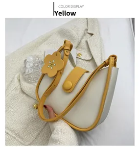 Detail of cream half-moon crossbody bag with yellow trim and floral charm on tweed fabric