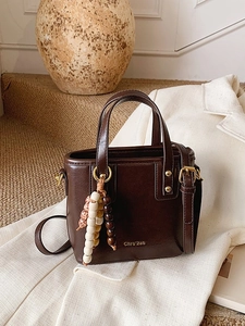 Sac seau marron chocolat minimaliste avec perles bohèmes sur un blazer blanc cassé