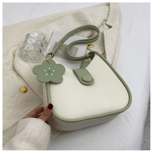 Close-up of cream and sage green leather saddle bag with floral charm on textured fabric