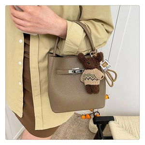 Vue détaillée du sac seau en cuir grainé marron foncé avec un accessoire de charme ours