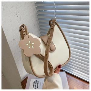 Detail of off-white saddle bag with brown trim and floral leather charm accessory