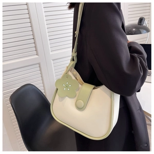 Detail of cream and green crossbody bucket bag with floral charm on a black blazer