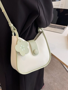 Minimalist beige and sage green shoulder bag with flower charm shown in office setting