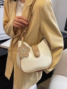 Minimalist beige crossbody bucket bag with brown trim and floral charm detail