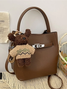 Sac seau en cuir marron avec fermoir argenté et charm ours en peluche dans un cadre doux
