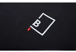 Macro shot of precise white letter B embroidery on black cotton t-shirt fabric