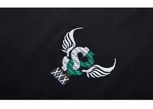 Close-up of high-density embroidery featuring wings and green motifs on black cotton fabric