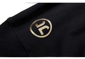 Detailaufnahme des goldenen Logos auf schwarzem Baumwollstoff mit Rippbündchen für Hoodies