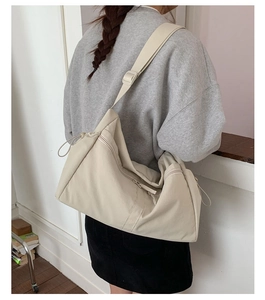 Detail of a large beige crossbody bag with zipper and drawstring shown on a model