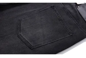 Macro detail of charcoal grey denim jeans featuring a leather patch and double-stitched pocket