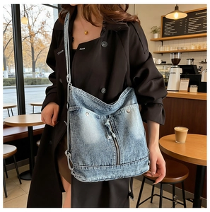 Détail d'un sac hobo en denim bleu clair avec délavage vintage et fermetures éclair décoratives