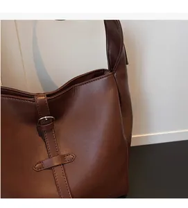 Close-up of brown leather shoulder bag featuring decorative buckle and soft texture