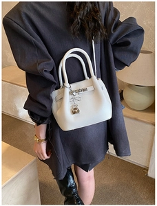Detail of white bucket bag with pebble leather texture and metallic heart pendant