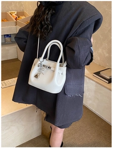 Detail of white lychee leather bucket bag with metal lock and bow ornament in street style