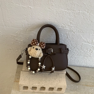 Detail of coffee brown mini bag with lychee texture and plush bear charm on stone base