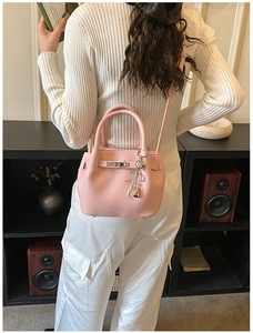 Detail of light pink lychee texture bucket bag with metal turn-lock and heart pendant