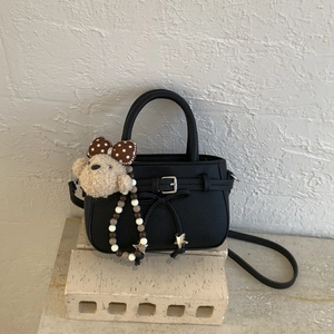 Detail of black pebbled leather handbag with silver buckle and cute plush bear charm