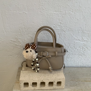 Detail of taupe pebbled handbag with star charm and plush dog pendant on stone